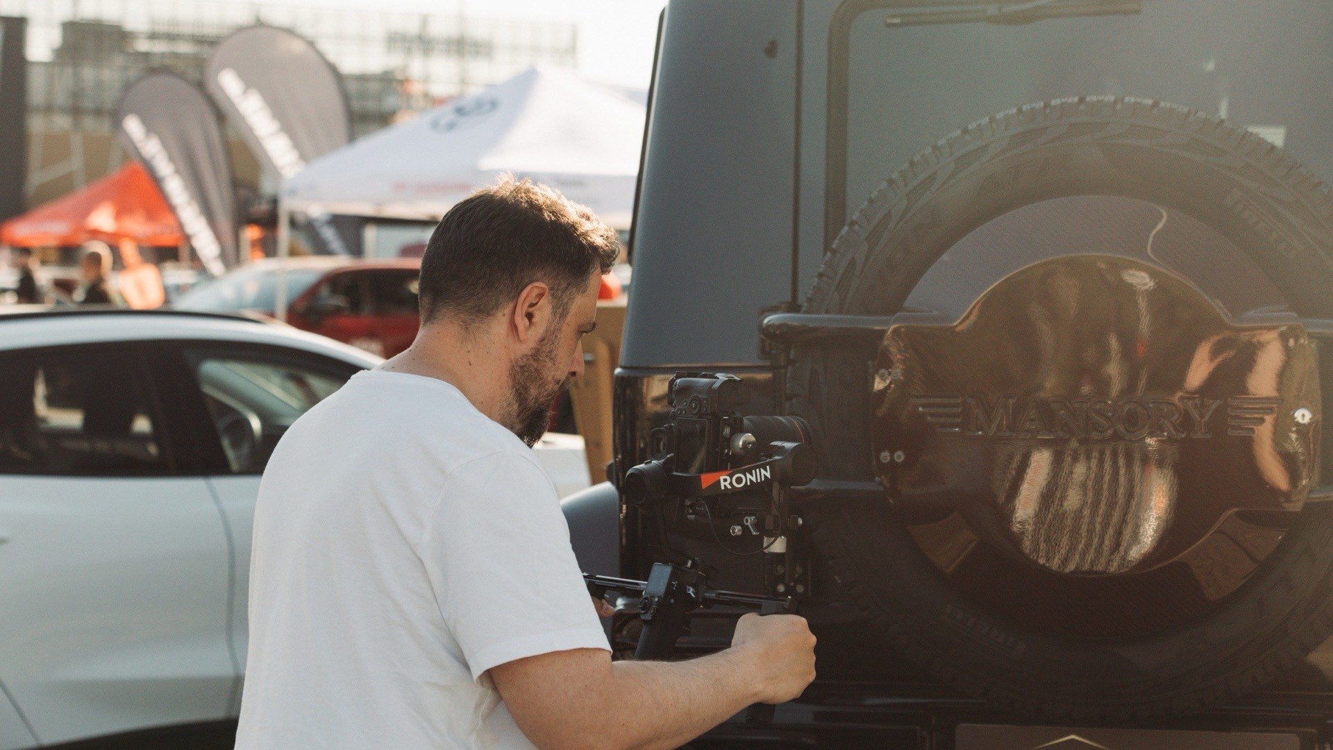 Operator filmând cu rig stabilizat lângă un Land Rover Defender, la un eveniment auto
